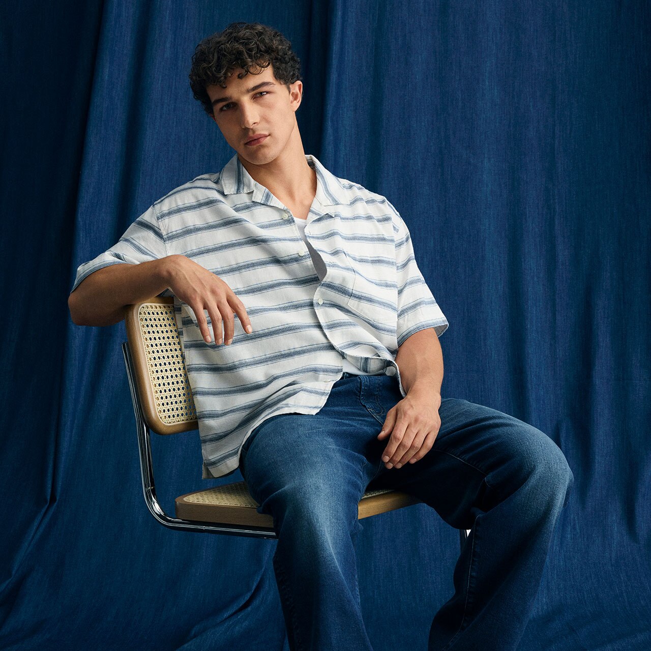 Modelo hombre usando camisa con rayas horizontales y pantalón azul marino de mezclilla. Pulsa aquí para ver camisas de la marca American Eagle.