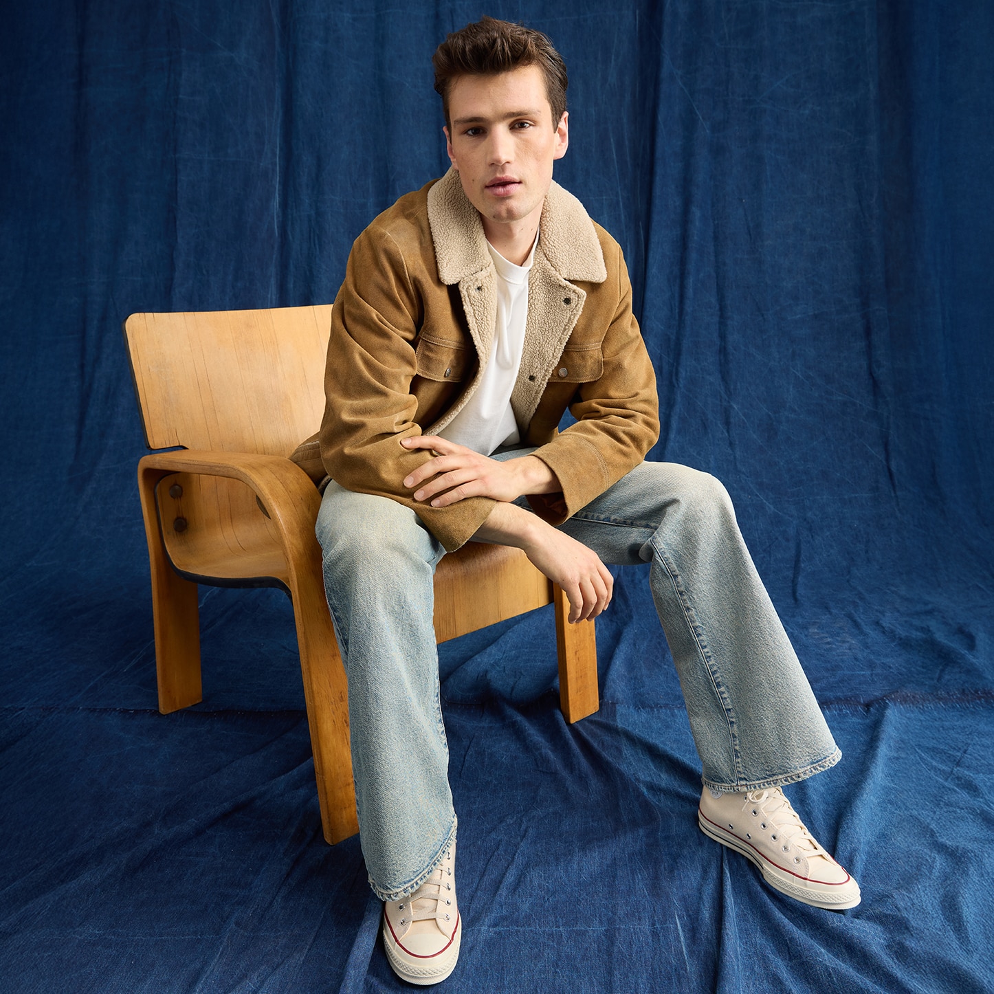 Modelo hombre usando chamarra color caqui con playera blanca, pantalón azul deslavado y tenis blancos. Pulsa aquí para ver ropa para hombre de la marca American Eagle.