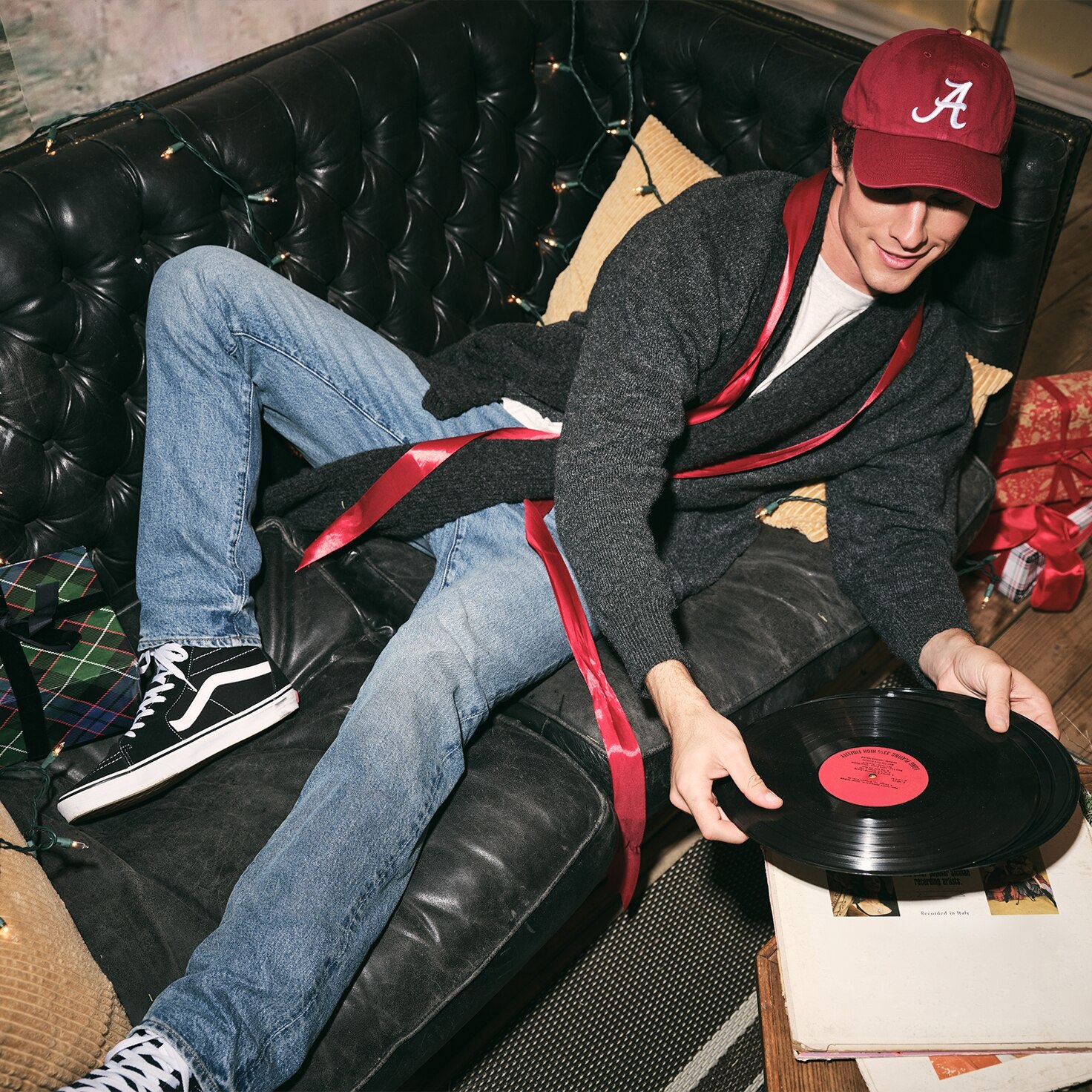 Modelo hombre usando abrigo negro, gorra roja y pantalón de mezclilla azul. Pulsa aquí para ver ropa American Eagle para hombre.