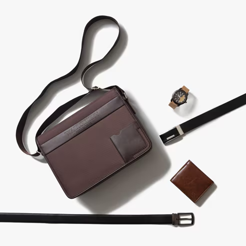 Composición de accesorios para hombre que incluye maletín café de hombro, con detalles en material tipo cuero en la parte frontal; cinturón café oscuro, cartera café para caballero y reloj análogo de mano. Pulsa aquí para conocer más de los productos Wallstreet, abre en pestaña nueva.